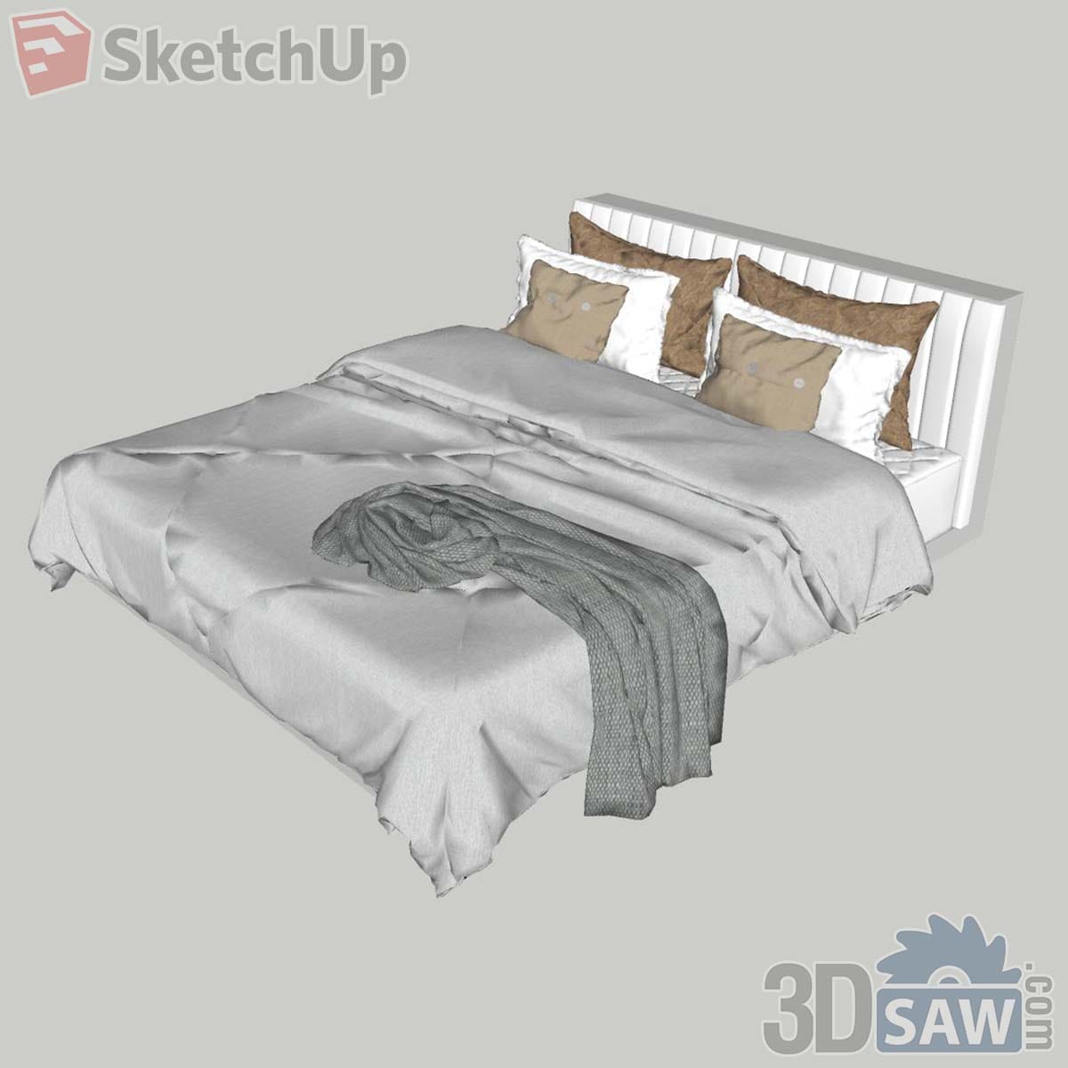 White channel-tufted bed with grey duvet, tan pillows and a crumpled knitted throw